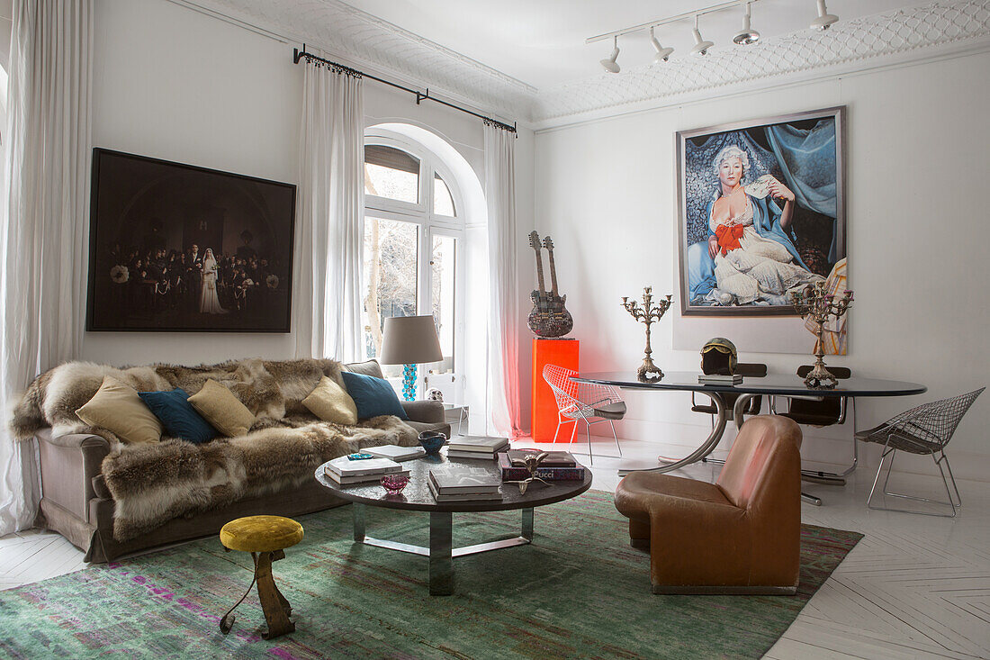 Sofa with fur blanket and cushions, coffee table and armchair, in the background 70s dining table under a painting