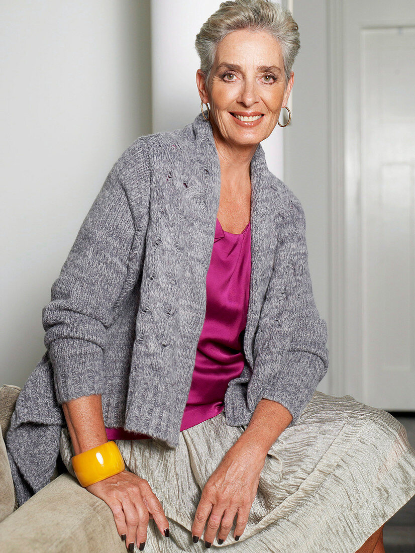 A grey-haired woman wearing a pink top, a grey cardigan and a skirt