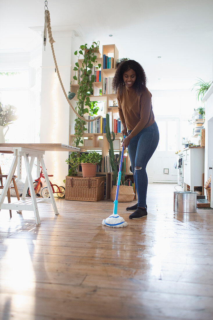 Woman mopping hardwood floor in apartment