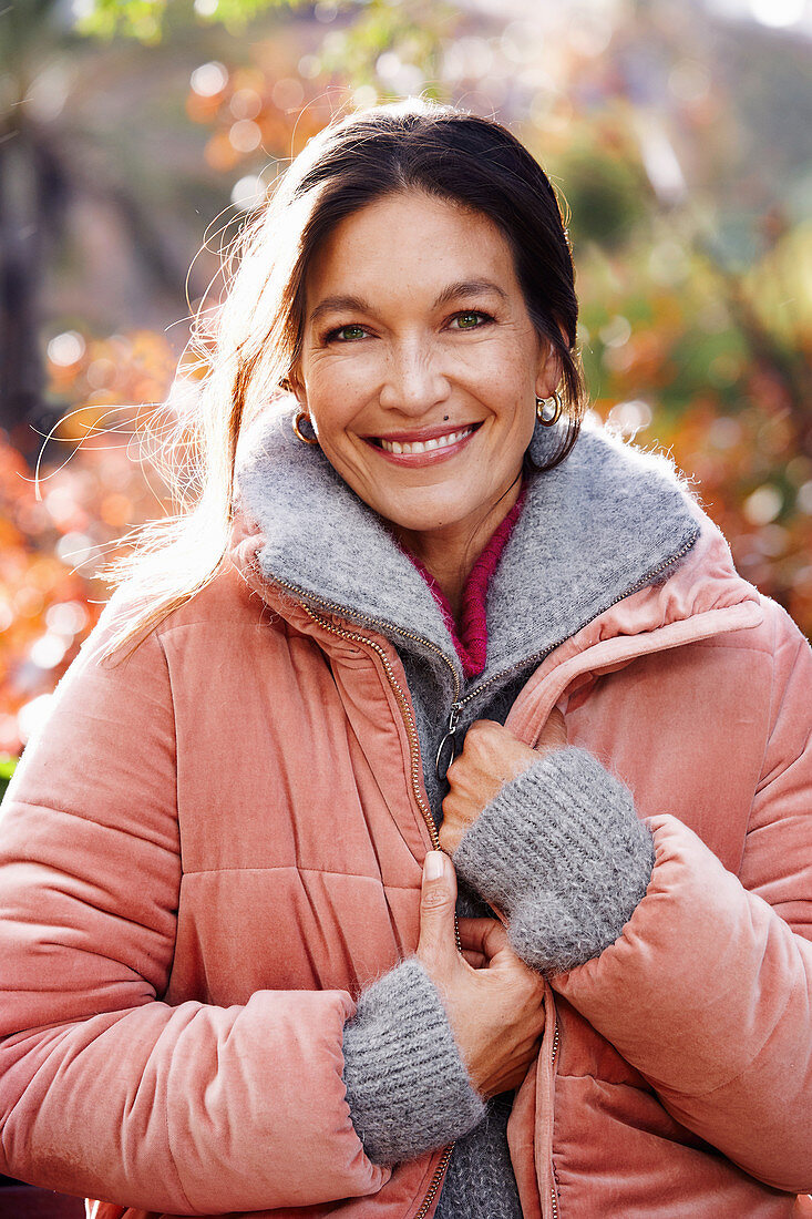 A dark-haired woman wearing a grey cardigan and a pink quilted jacket