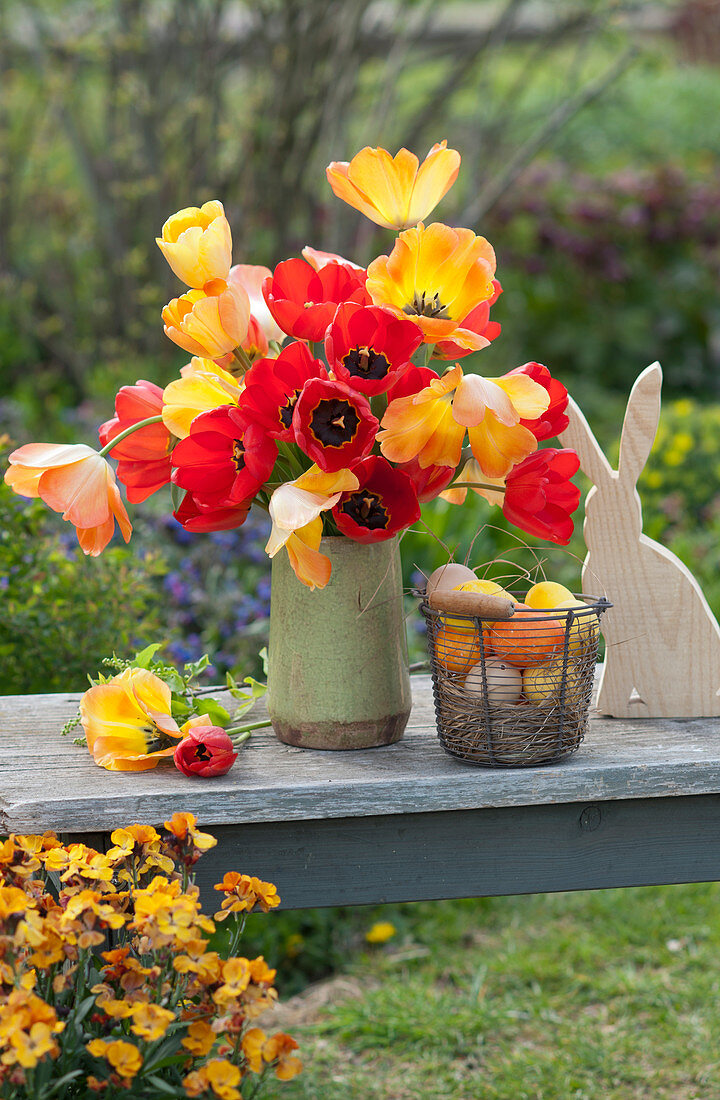 Easter bouquet of red and orange tulips, wooden Easter bunny, and Easter eggs in a wire basket