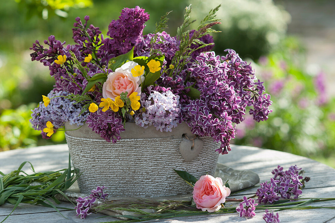 Flower arrangement with lilacs, Chippendale roses, grass, and buttercups in a planter with a heart pendant