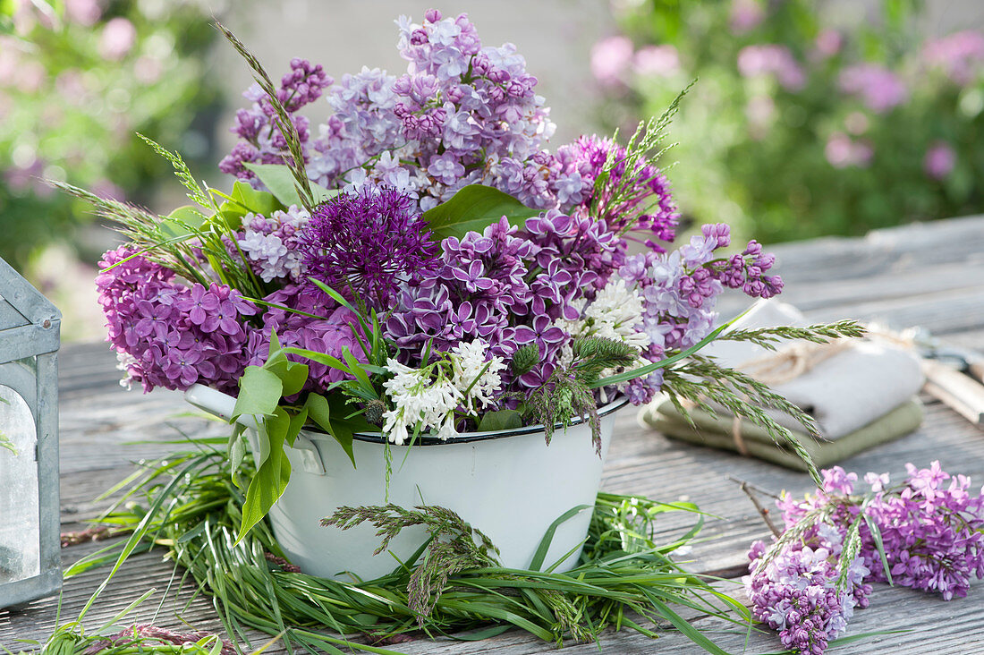 Arrangement of lilac, allium, and grass in an enamel pot surrounded by a grass wreath