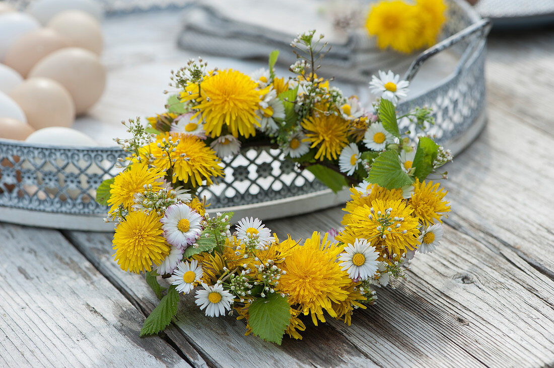Wreath of dandelions, daisies, and field pennycress on a tray with Easter eggs