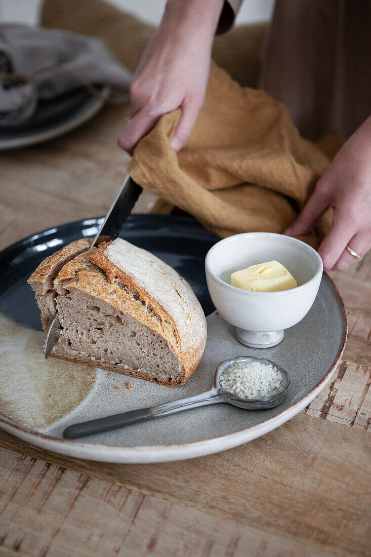 Bread being cut on ceramic plate with butter