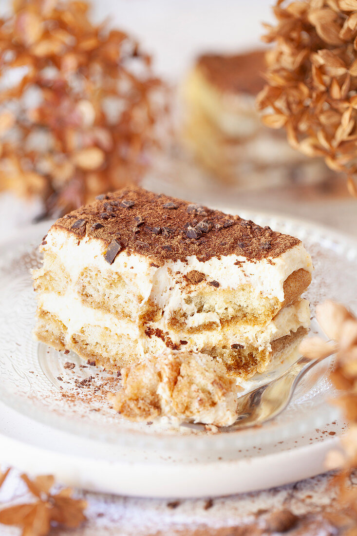 A slice of part eaten tiramisu dessert on a glass plate