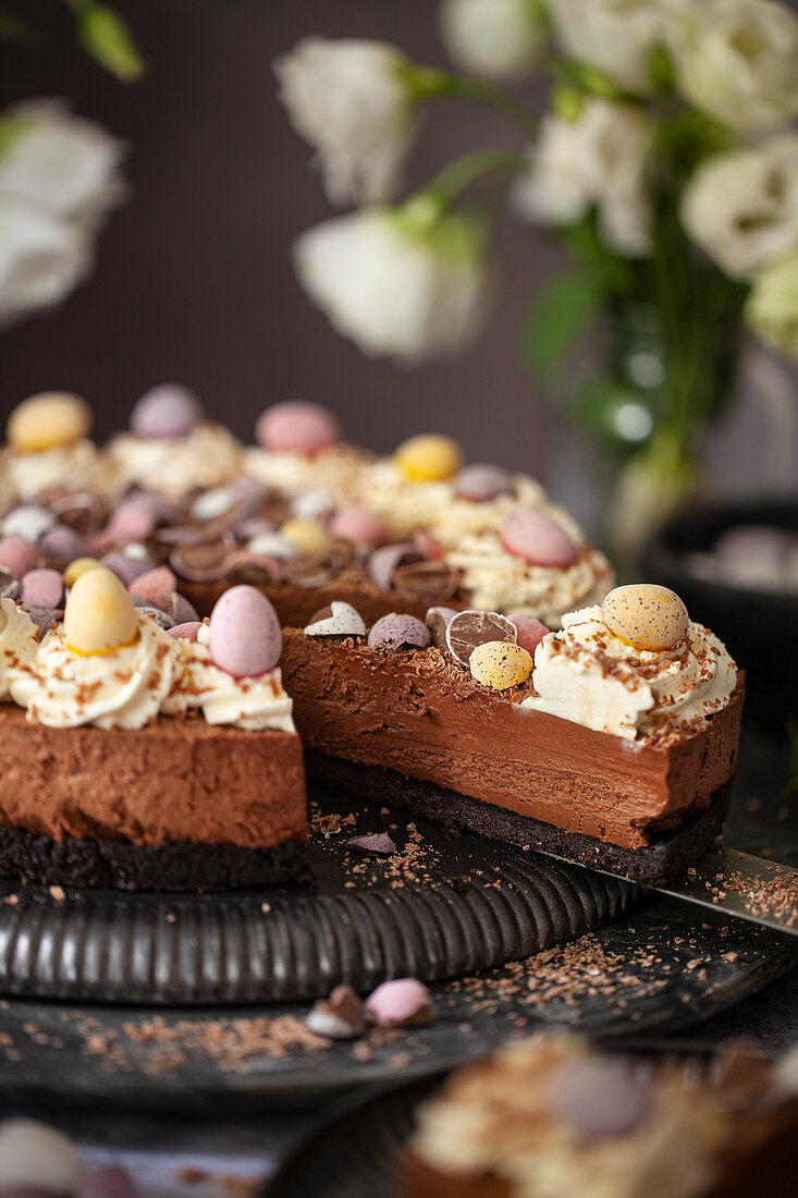 Serving slices of a no-bake chocolate cheesecake decorated with whipped cream, chocolate flakes and candy Easter eggs