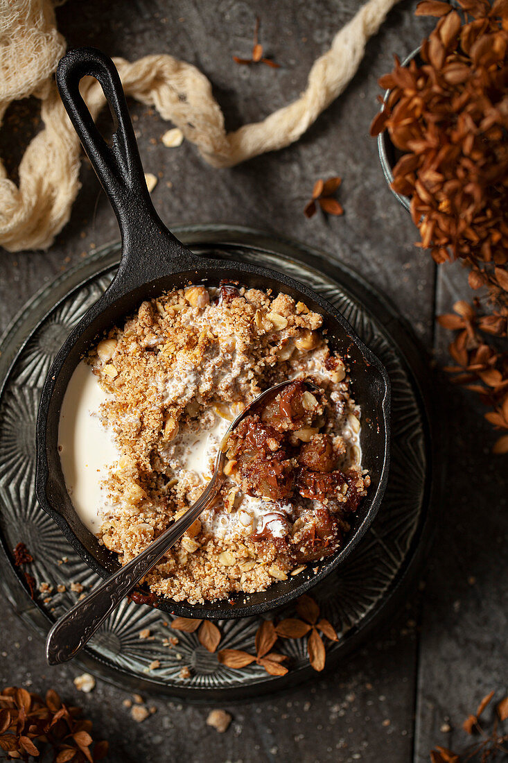 A single-serve cast iron skillet holding pear and chocolate crumble topped with cream