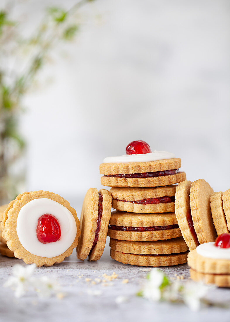 Jam filled shortbread cookies stack up, some with glaces icing and a cherry on the top to form Empire Biscuits