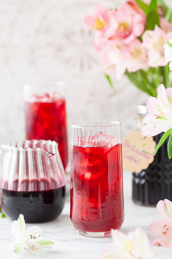 A glass filled with diluted blackcurrant cordial and ice with a jug of cordial next to it