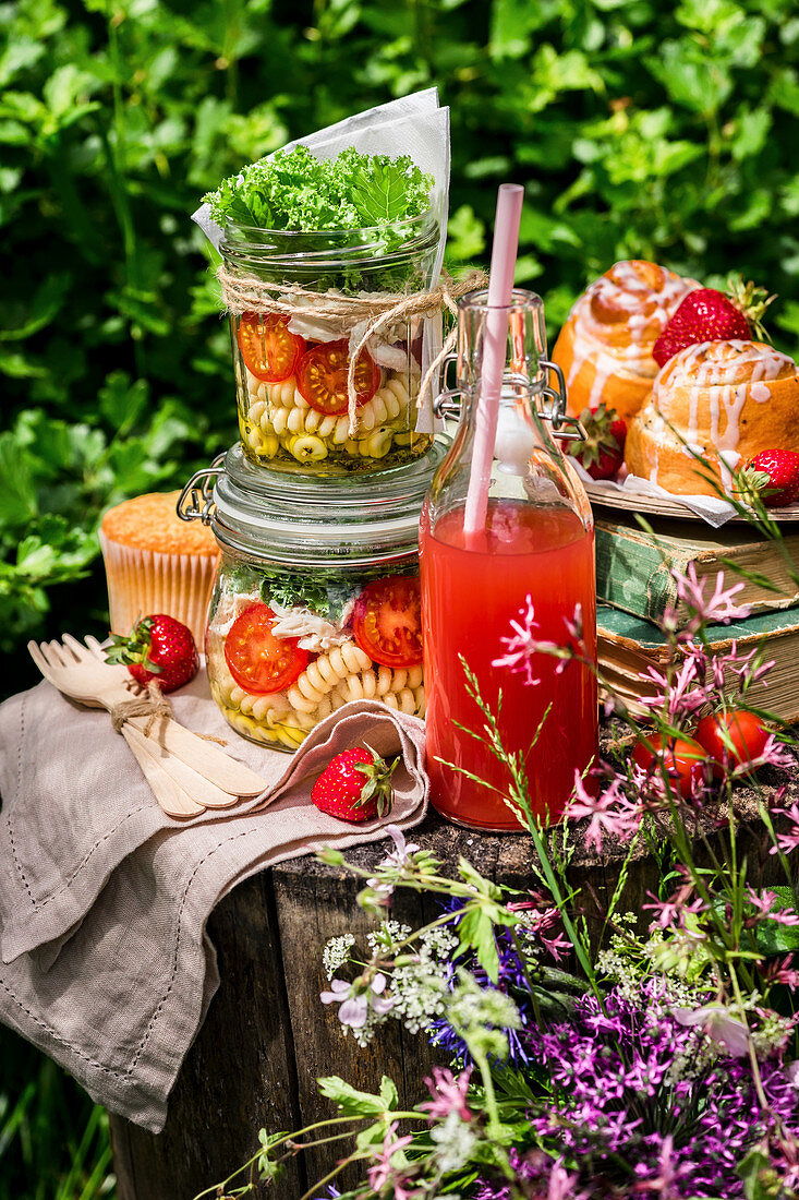 Salat in Gläsern, Limonade und Gebäck fürs Picknick auf Baumstumpf