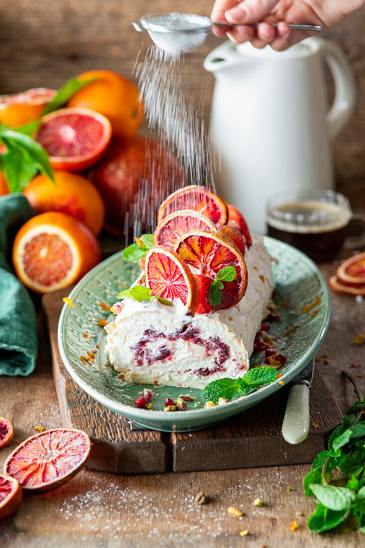 Blood orange meringue roll being dusted with icing sugar