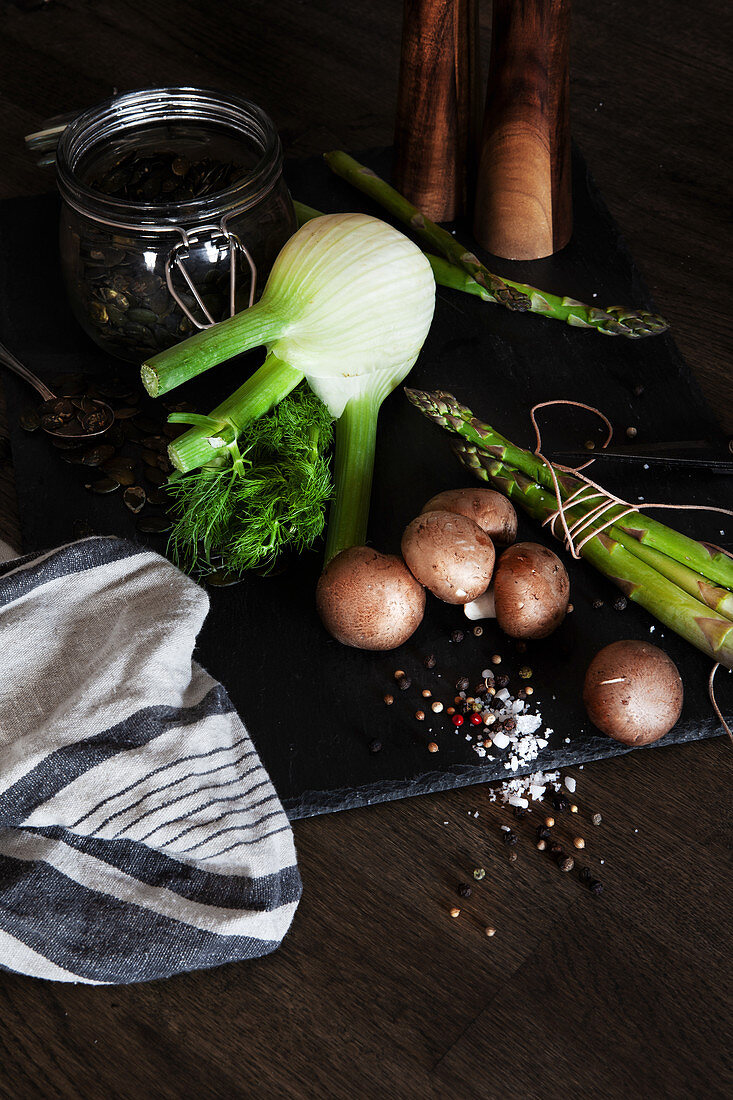 Stillleben mit Fenchel, grünem Spargel, braunen Champignons und Kürbiskernen