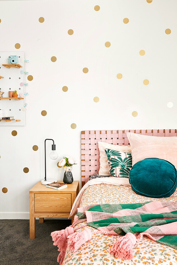 Bett mit Rosa Akzenten vor Wand mit goldfarbenen Punkten im Mädchenzimmer