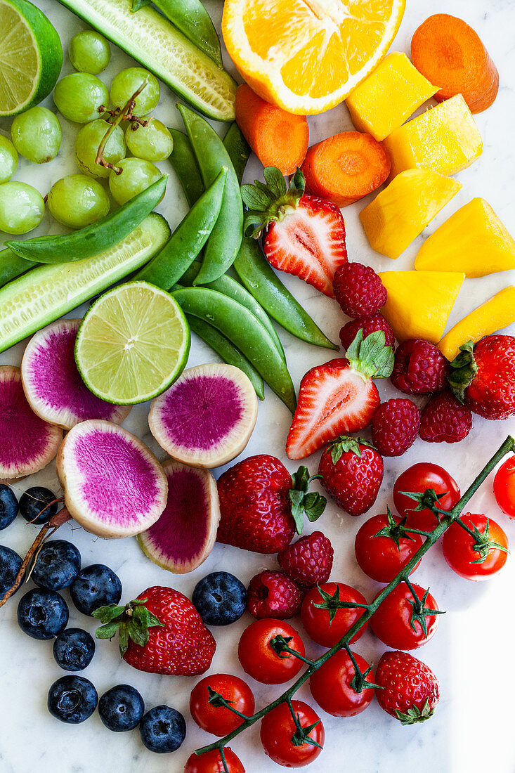 Various fruits and vegetables, arranged by colour on a marble countertop