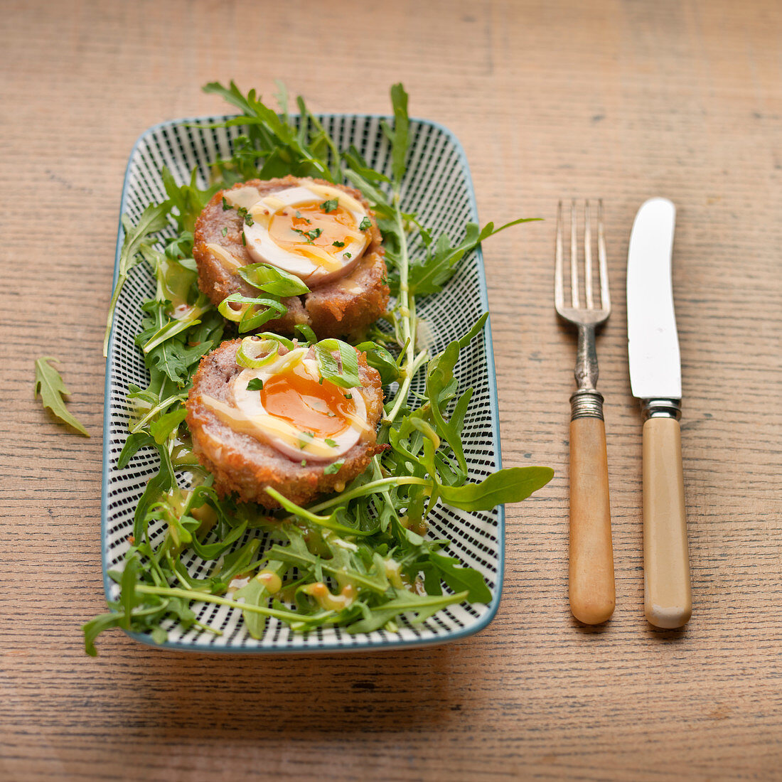 Two Scotch eggs with runny yokes on rocket salad