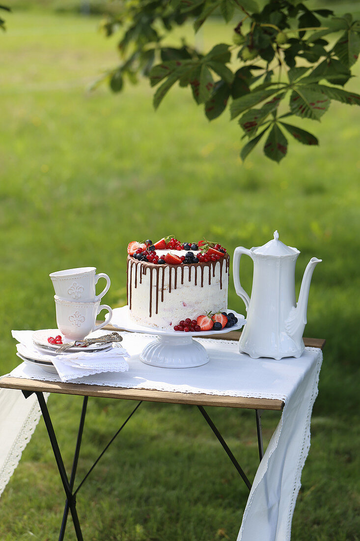 White drip cake with fresh berries on a table in the garden