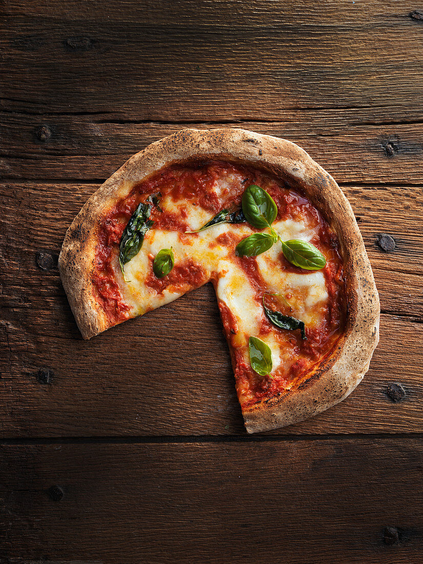 Pizza Margherita, angeschnitten auf Holzuntergrund