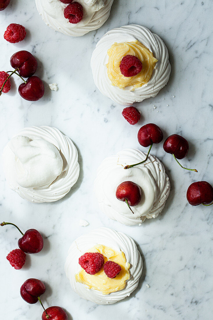 Individual meringues topped with lemon curd, raspberries, whipped cream and cherries
