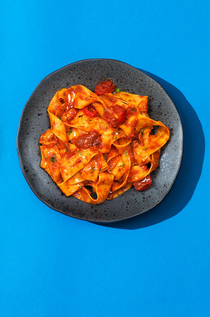 Ein Teller mit Tomaten-Pappardelle auf blauem Untergrund