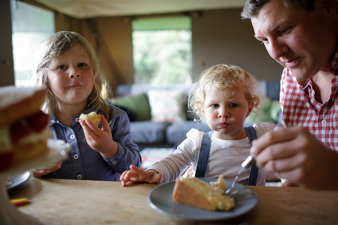 Father and daughters eating cake at dining table