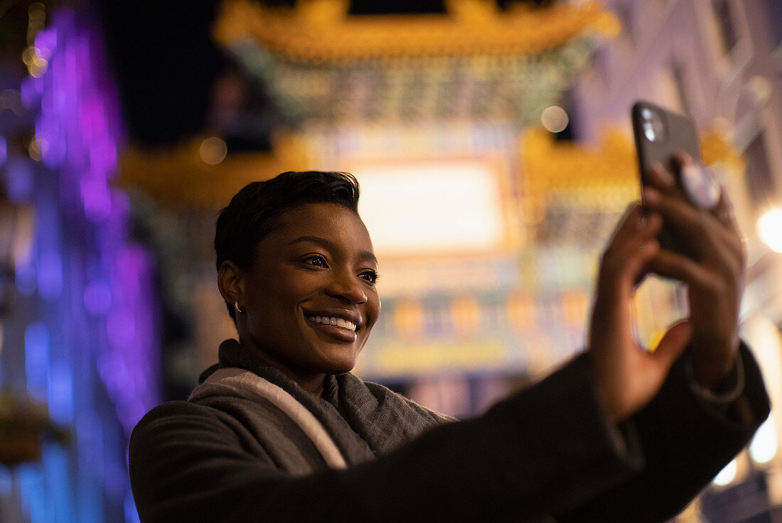 Happy young woman taking selfie in city at night