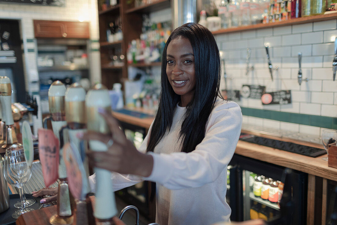 Happy young female bartender behind bar