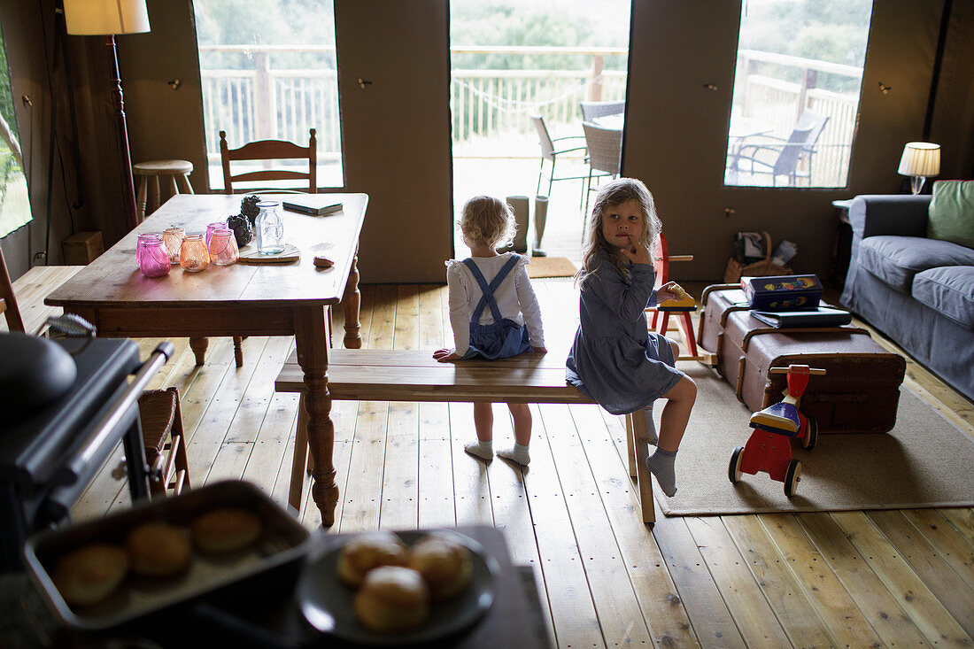 Sisters sitting on wood bench in dining room