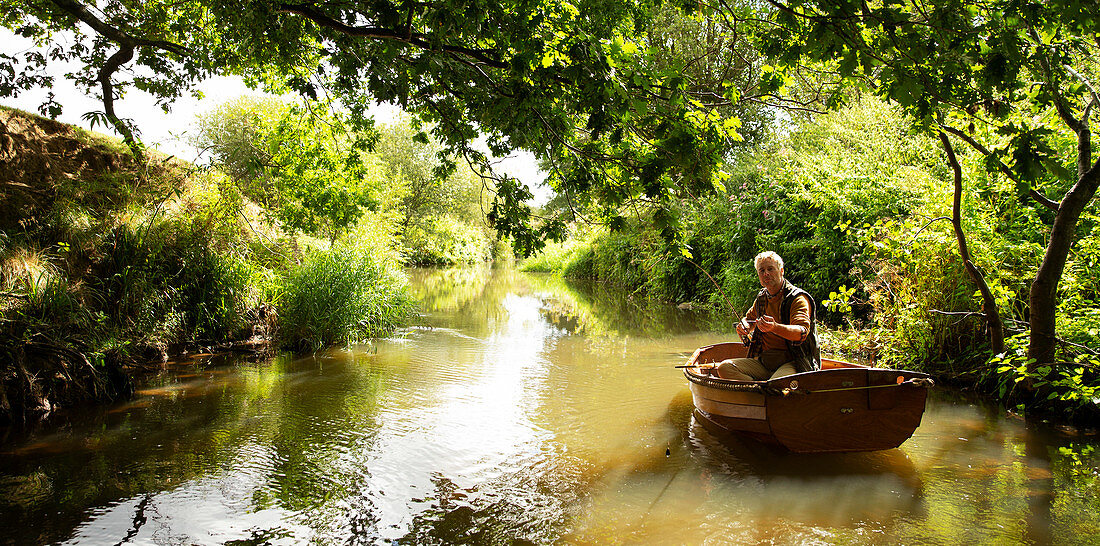 Man fly fishing from boat on tranquil green river