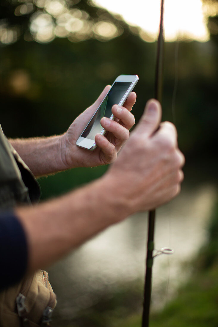 Man holding a fishing pole and smartphone