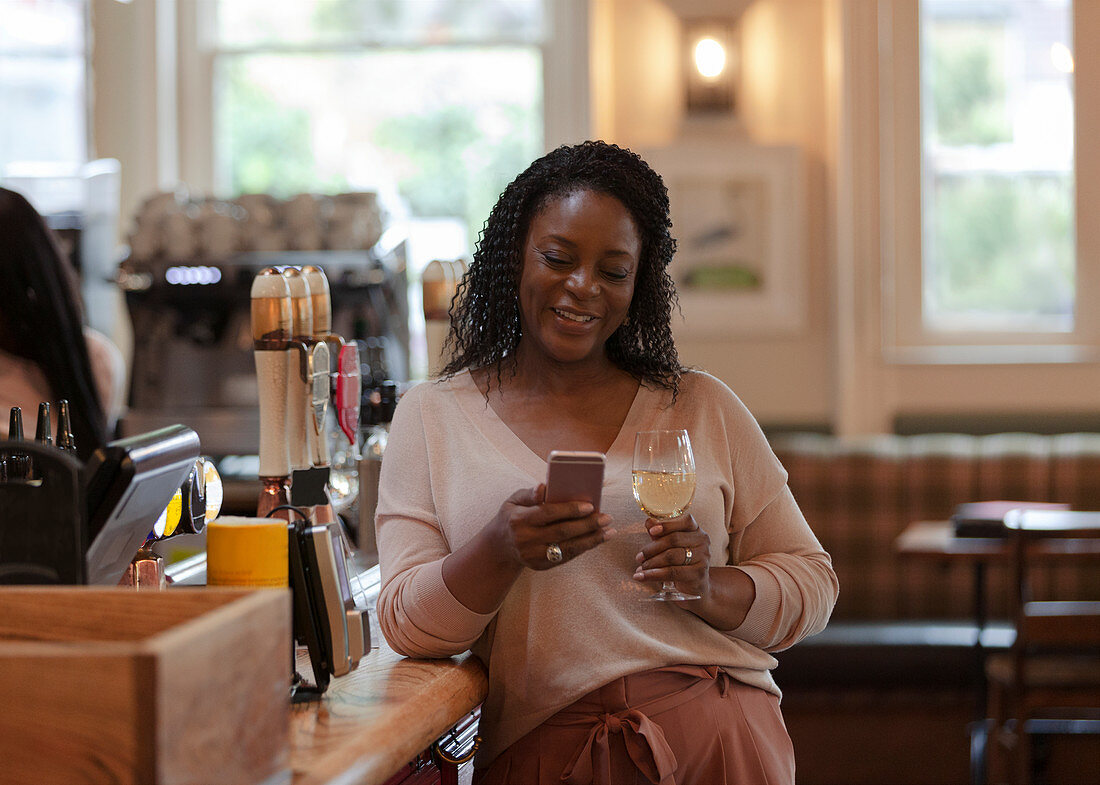 Woman with smartphone enjoying white wine in bar