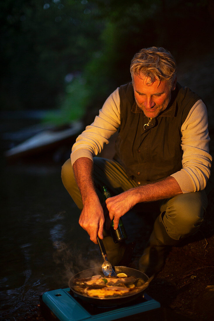 Man cooking freshly caught fish at dark riverbank