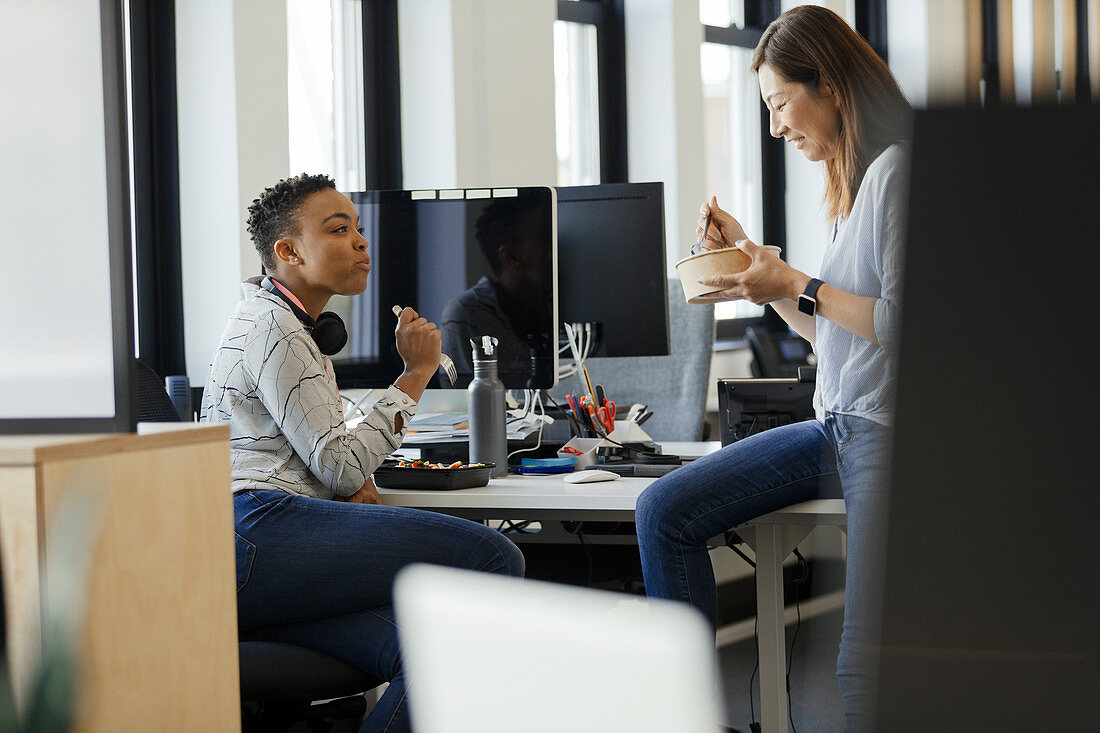 Businesswomen eating takeout lunch at desk in office