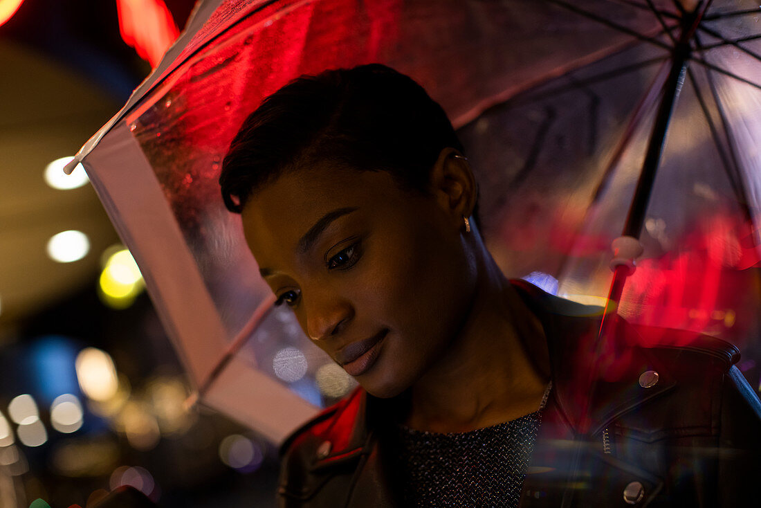 Young woman under umbrella with neon lights at night