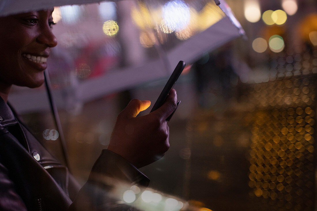 Young woman with smartphone under an umbrella at night