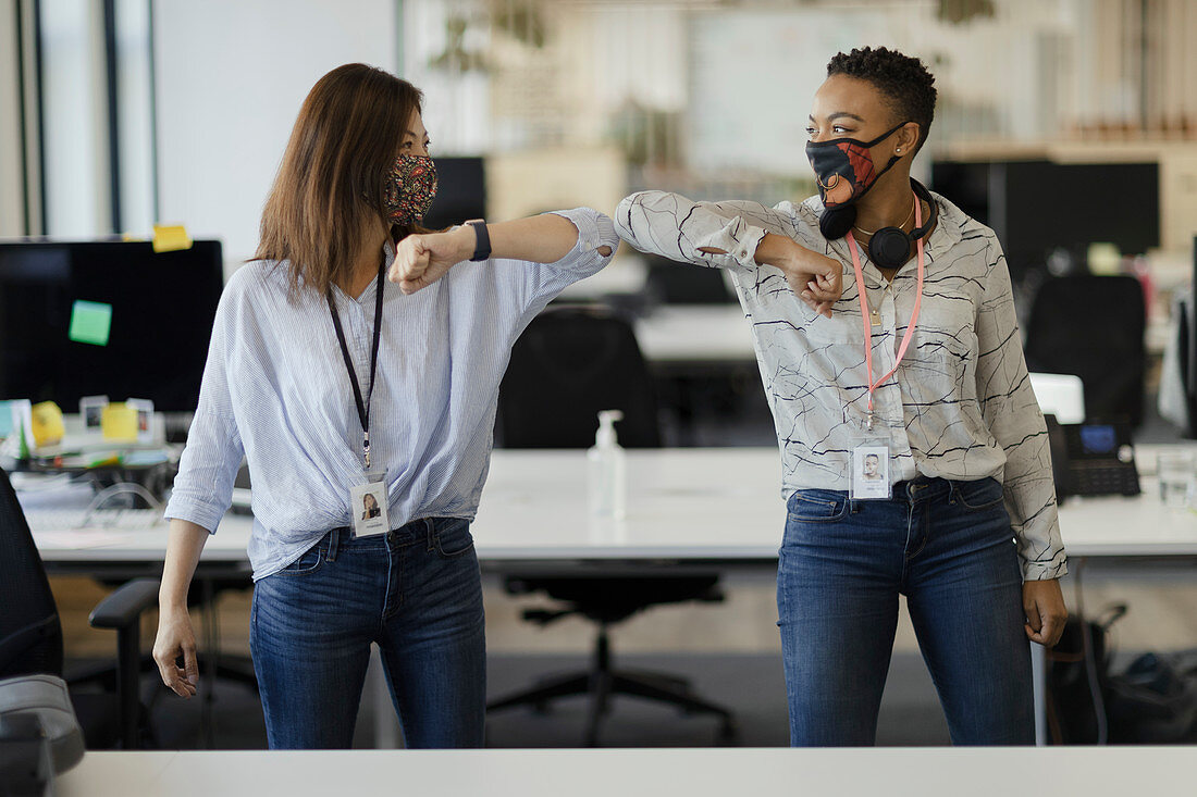 Businesswomen in face masks elbow bumping in office