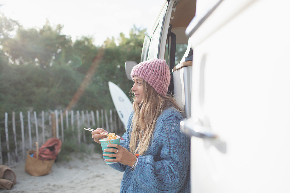 Young woman eating instant noodles outside camper van