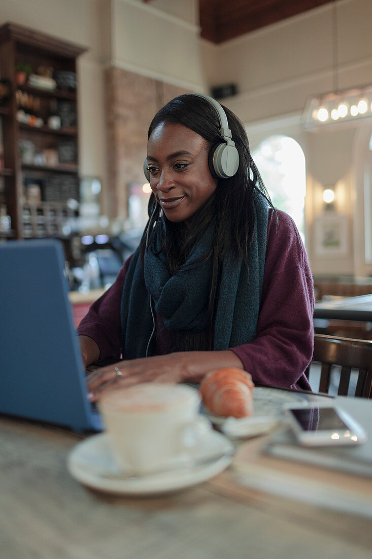 Young woman with headphones working at laptop in cafe