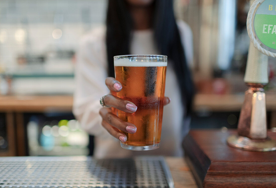 Female bartender serving pint of beer in pub
