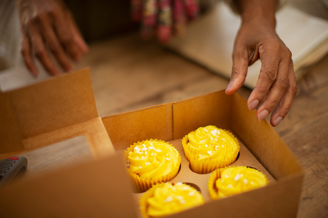 Woman reaching for lemon yellow cupcakes in bakery box