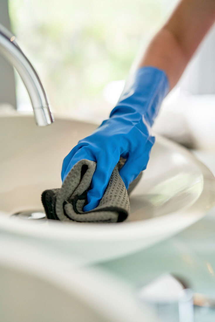 Hotel maid in gloves cleaning hotel room bathroom sink