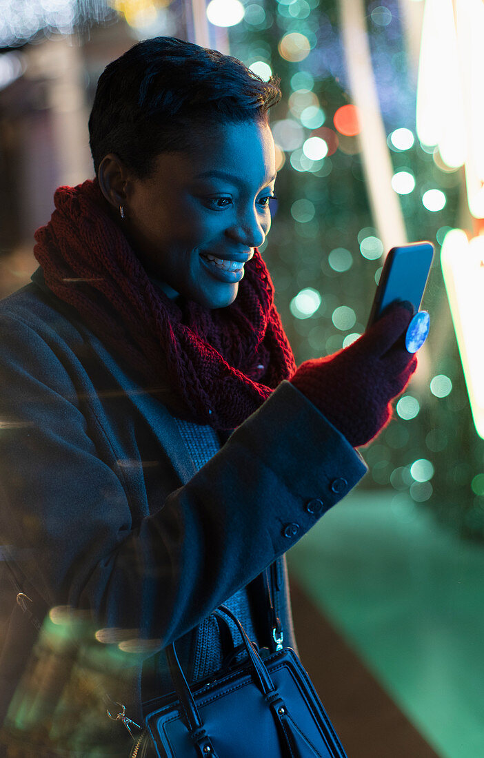 Young woman using smartphone on city sidewalk at night