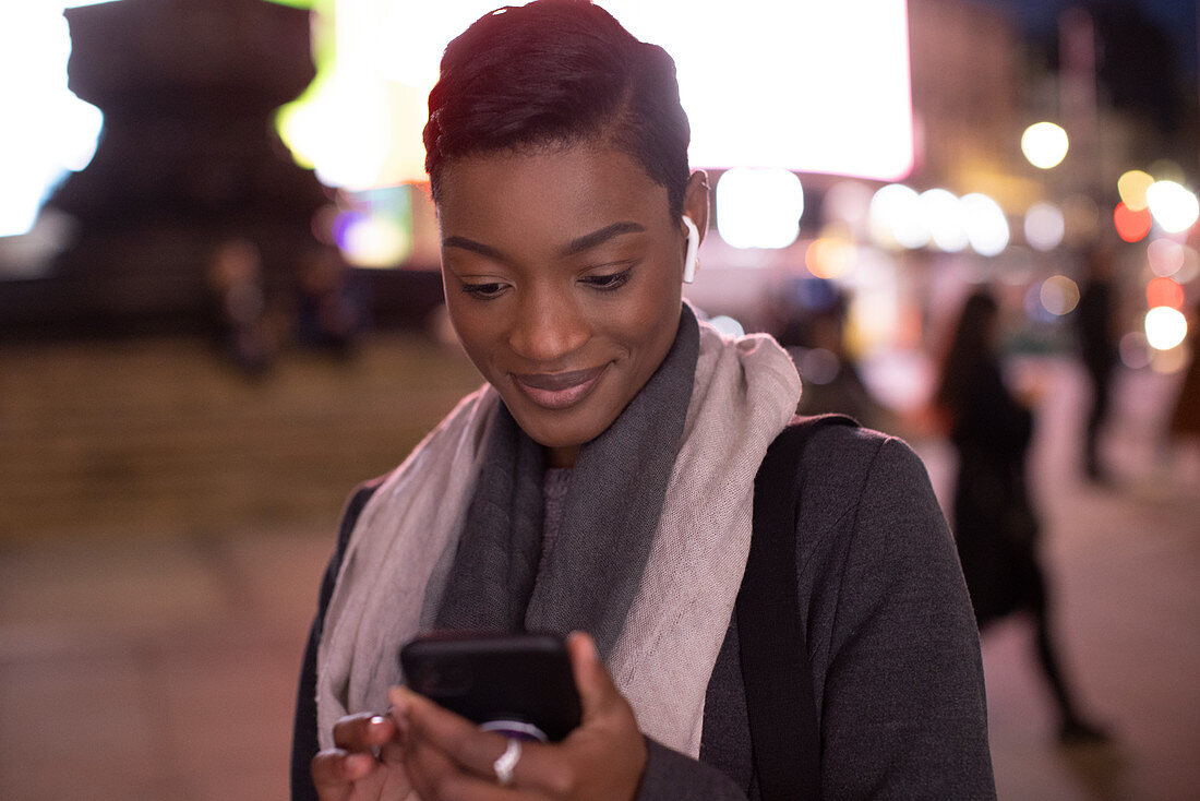 Young woman using smartphone on city sidewalk at night