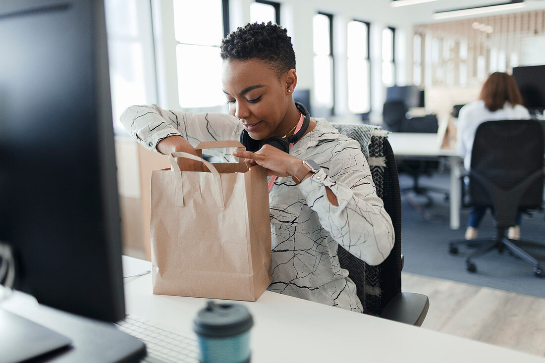Businesswoman opening takeout lunch bag at desk in office