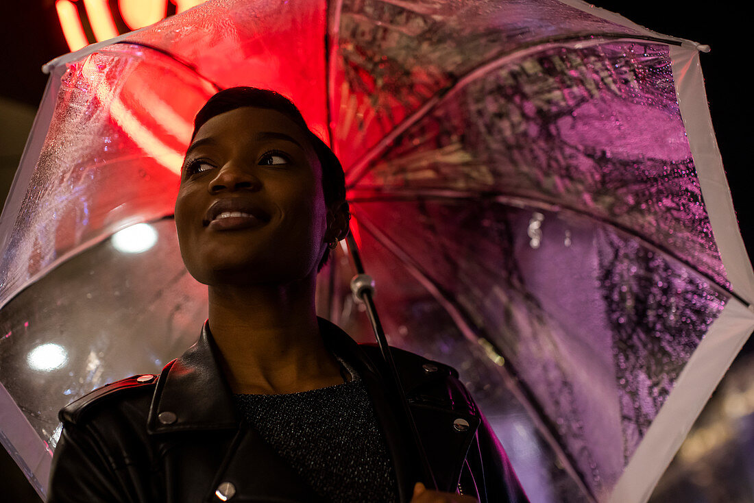 Smiling young woman under umbrella and neon sign at night