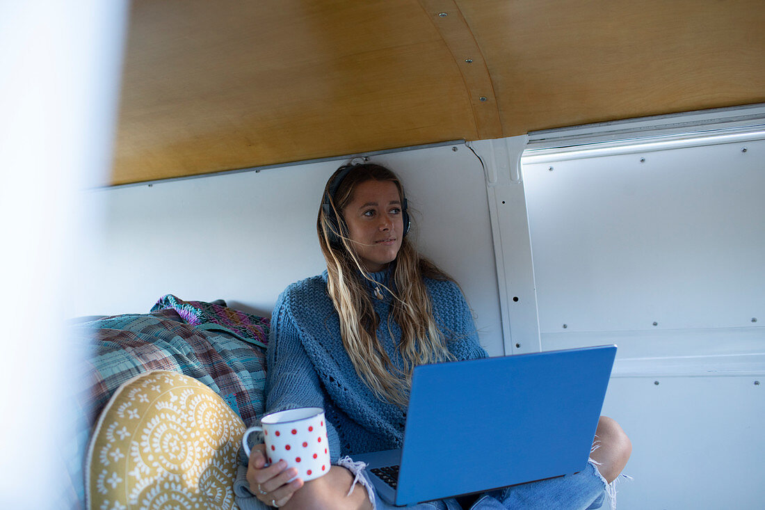 Carefree young woman with laptop and coffee in camper van