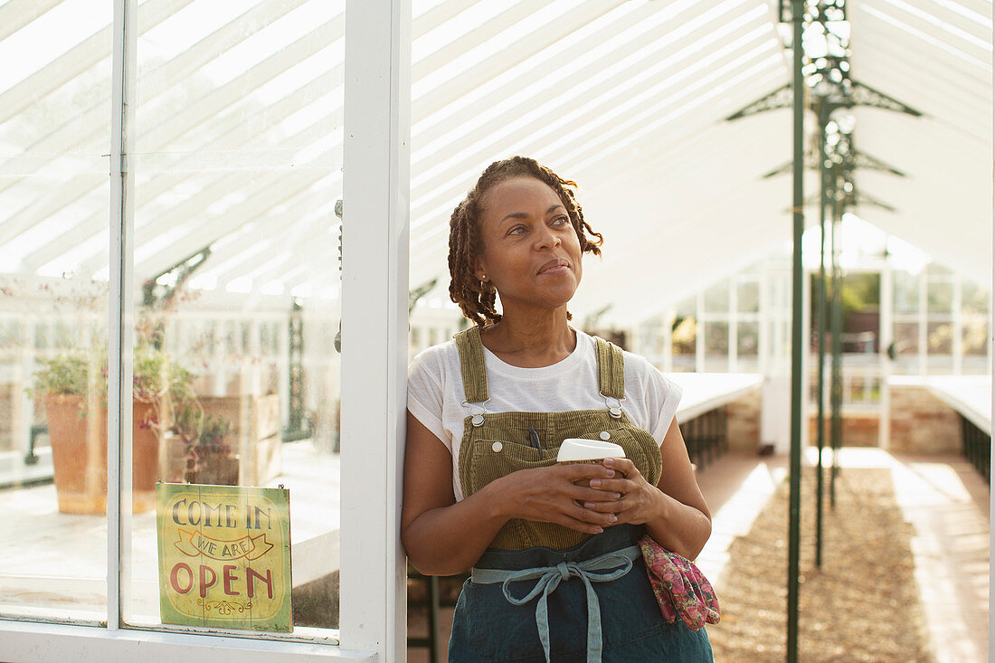 Garden shop owner with coffee in greenhouse doorway