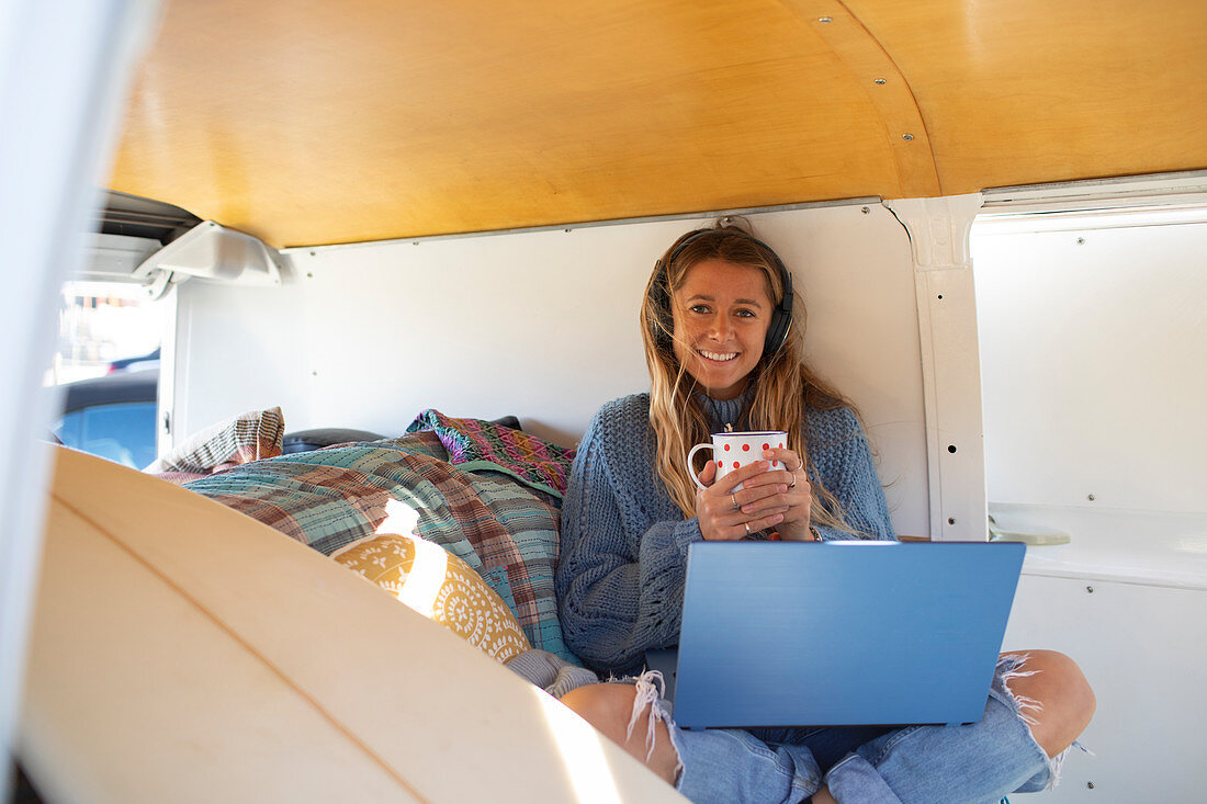 Happy young woman with laptop drinking tea in van