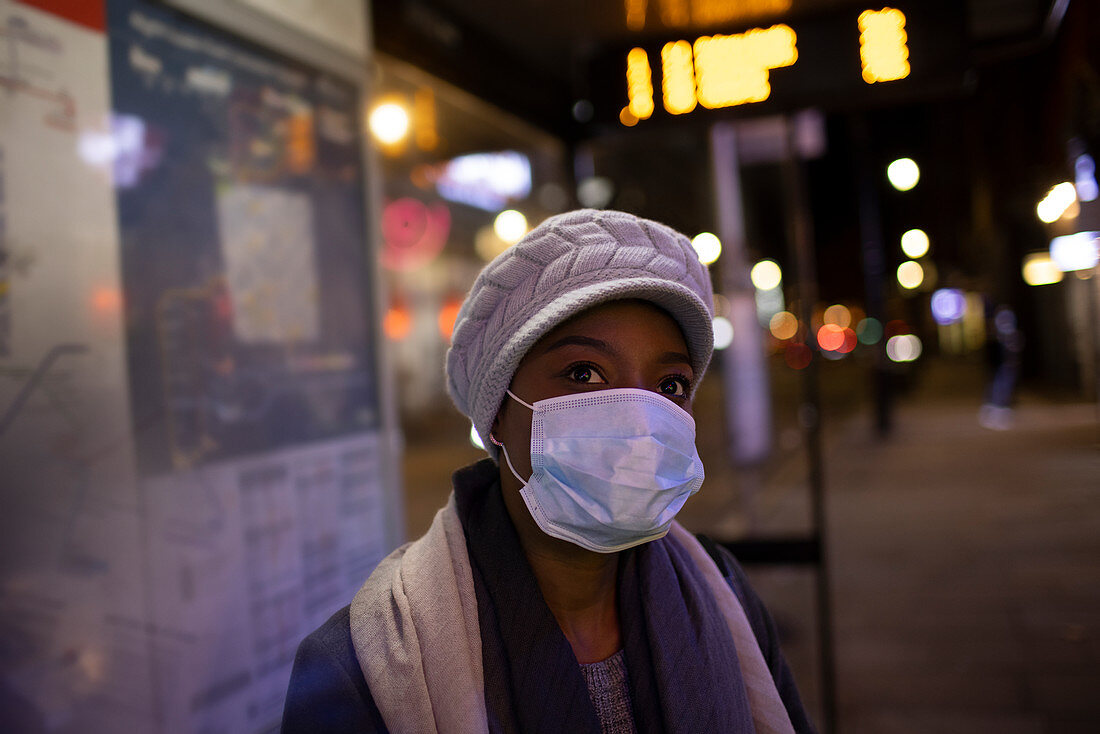 Young woman in face mask on city sidewalk at night