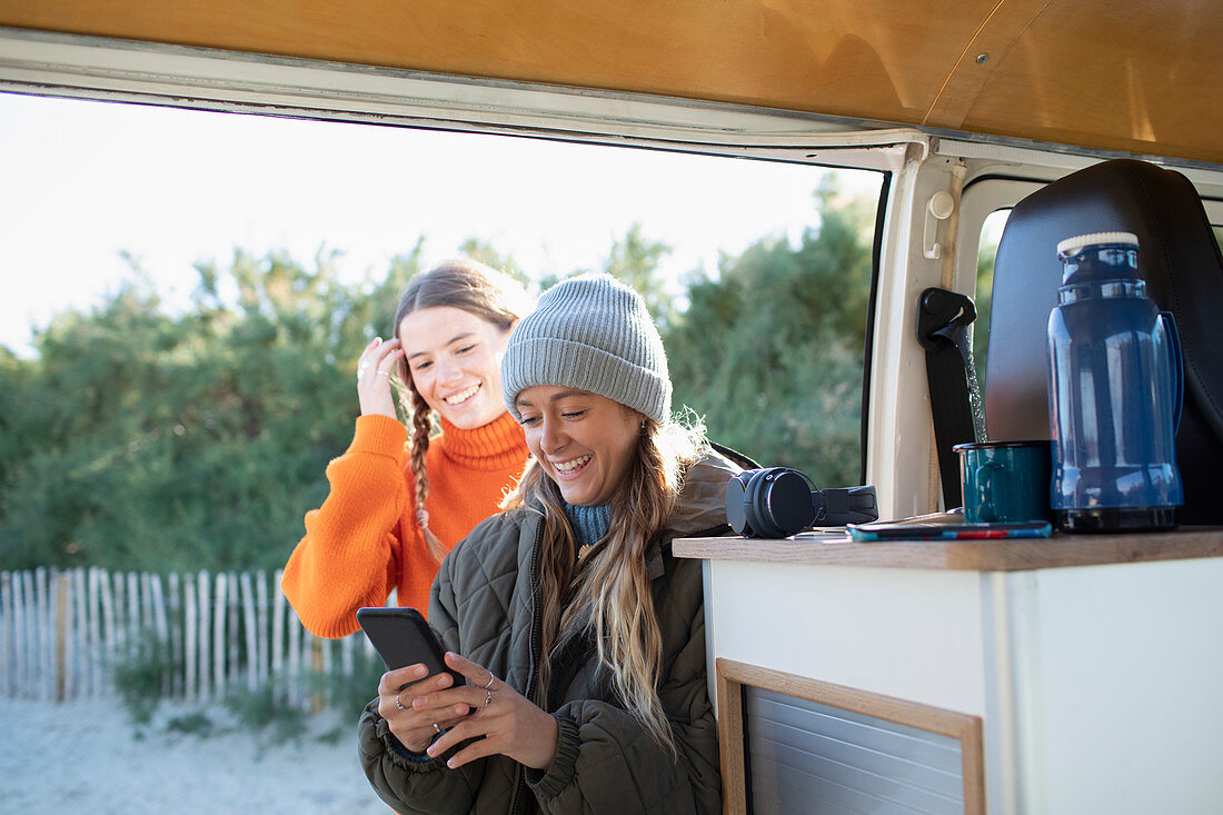 Young women friends using smartphone in camper van doorway
